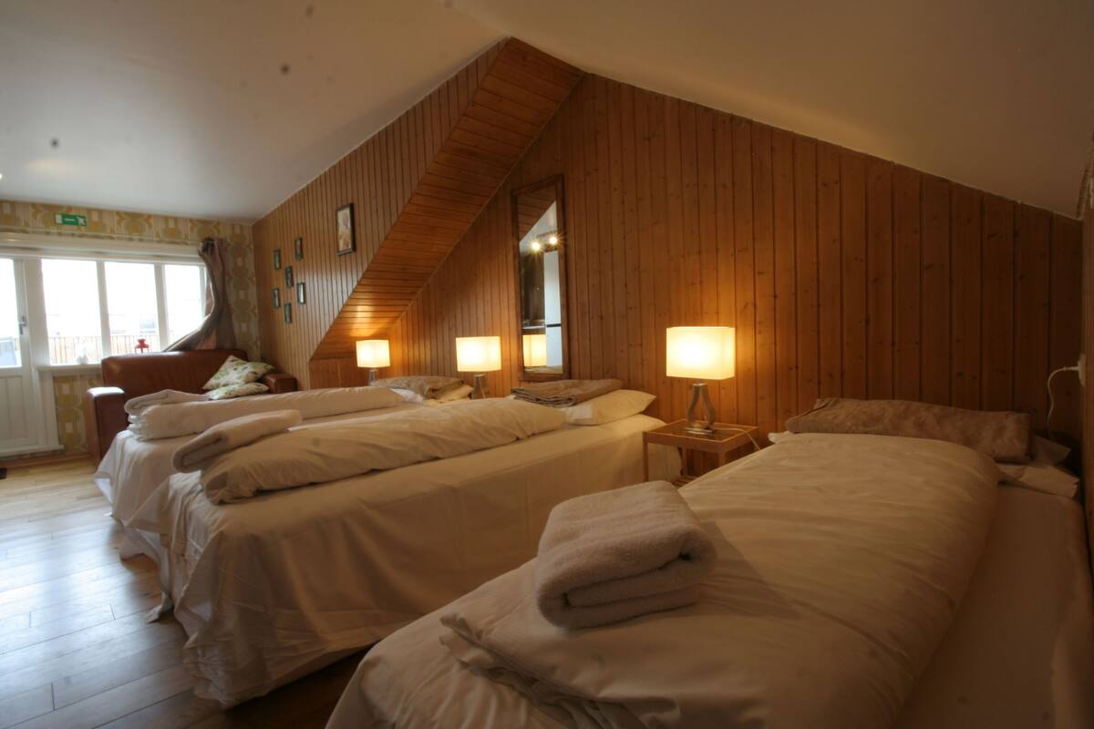 Habitación de hotel con tres camas, paredes de madera y techo inclinado.