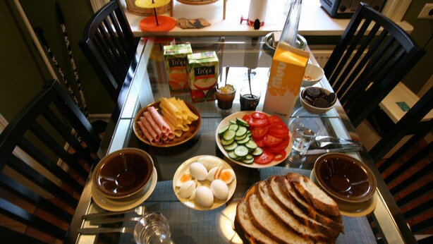 Et spisebord dækket med forskellig mad, blandt andet brød, æg, tomater og ost.