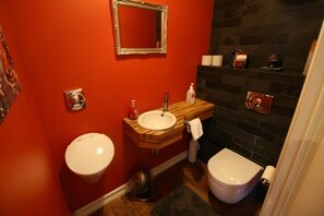 A bathroom with a red wall, a wooden vanity, a white sink, a toilet, and a mirror.