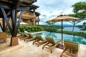A poolside area with lounge chairs and umbrellas, overlooking a lush landscape and a body of water.