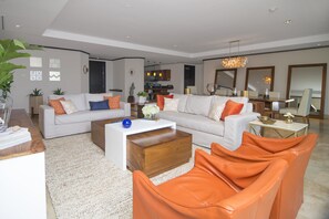 A modern living room with a sofa, coffee table, and orange chairs. There is a kitchen in the background.