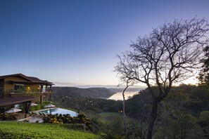 A modern house with a pool, surrounded by lush greenery and overlooking a lake.