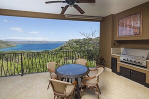 A balcony with a round table and chairs, a grill, and a view of a lake.