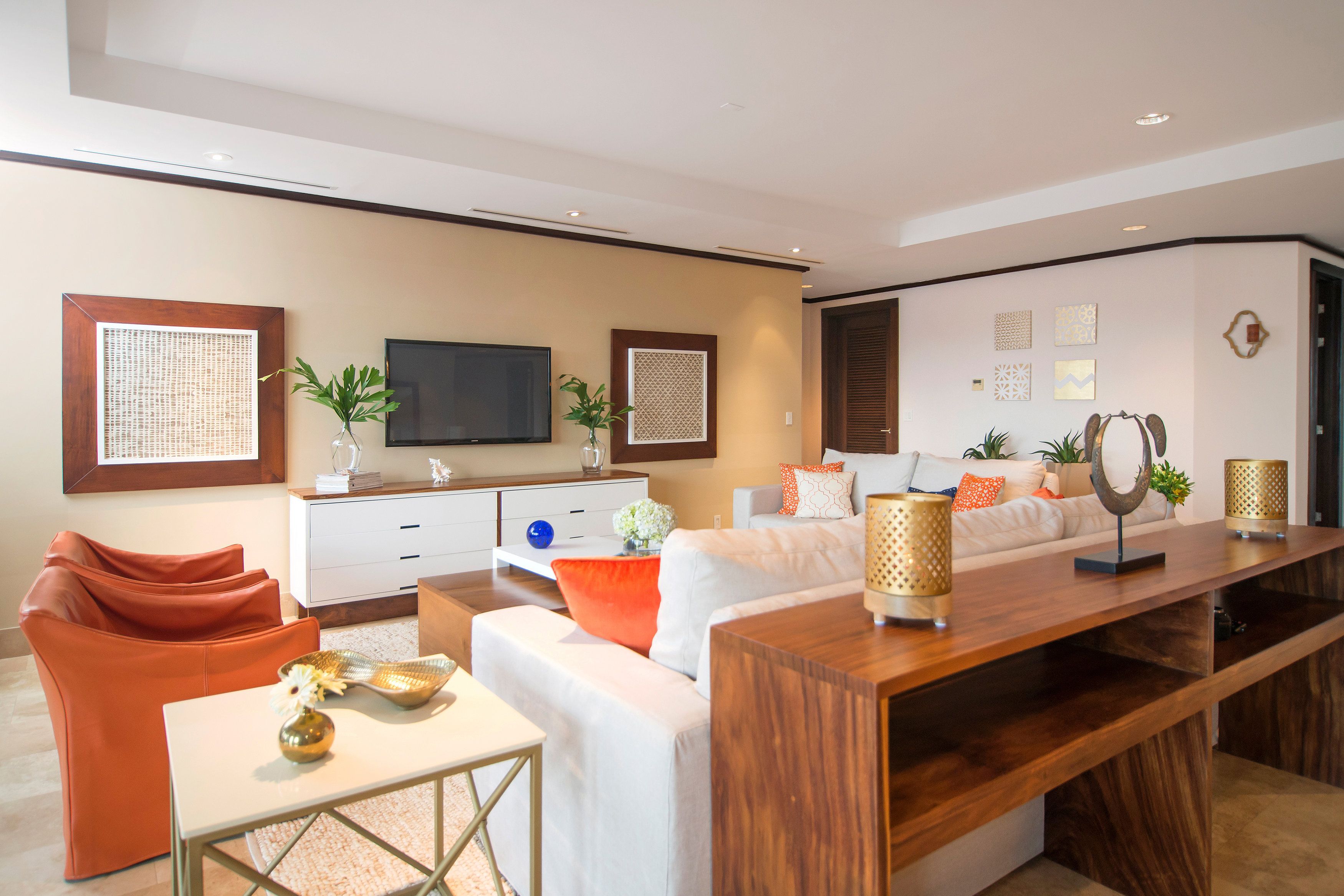 Una sala moderna con sofá, mesa de centro y televisor. Hay objetos decorativos y plantas en los estantes.