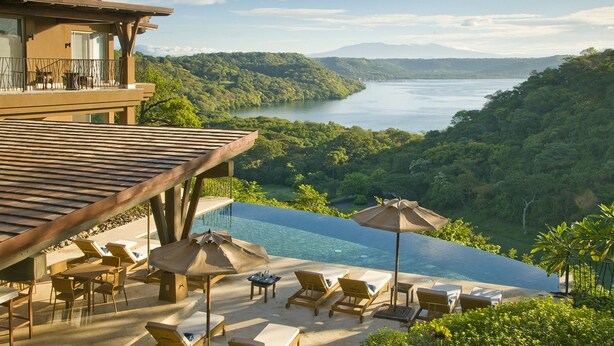 Uma villa luxuosa com piscina infinita privativa com vista para um lago, rodeada por vegetação exuberante.
