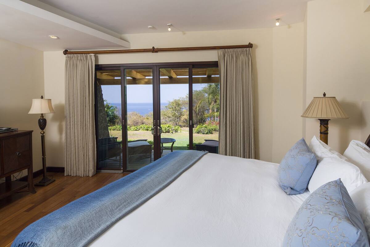 A bedroom with a large bed, a view of the outdoors, and a wooden floor.