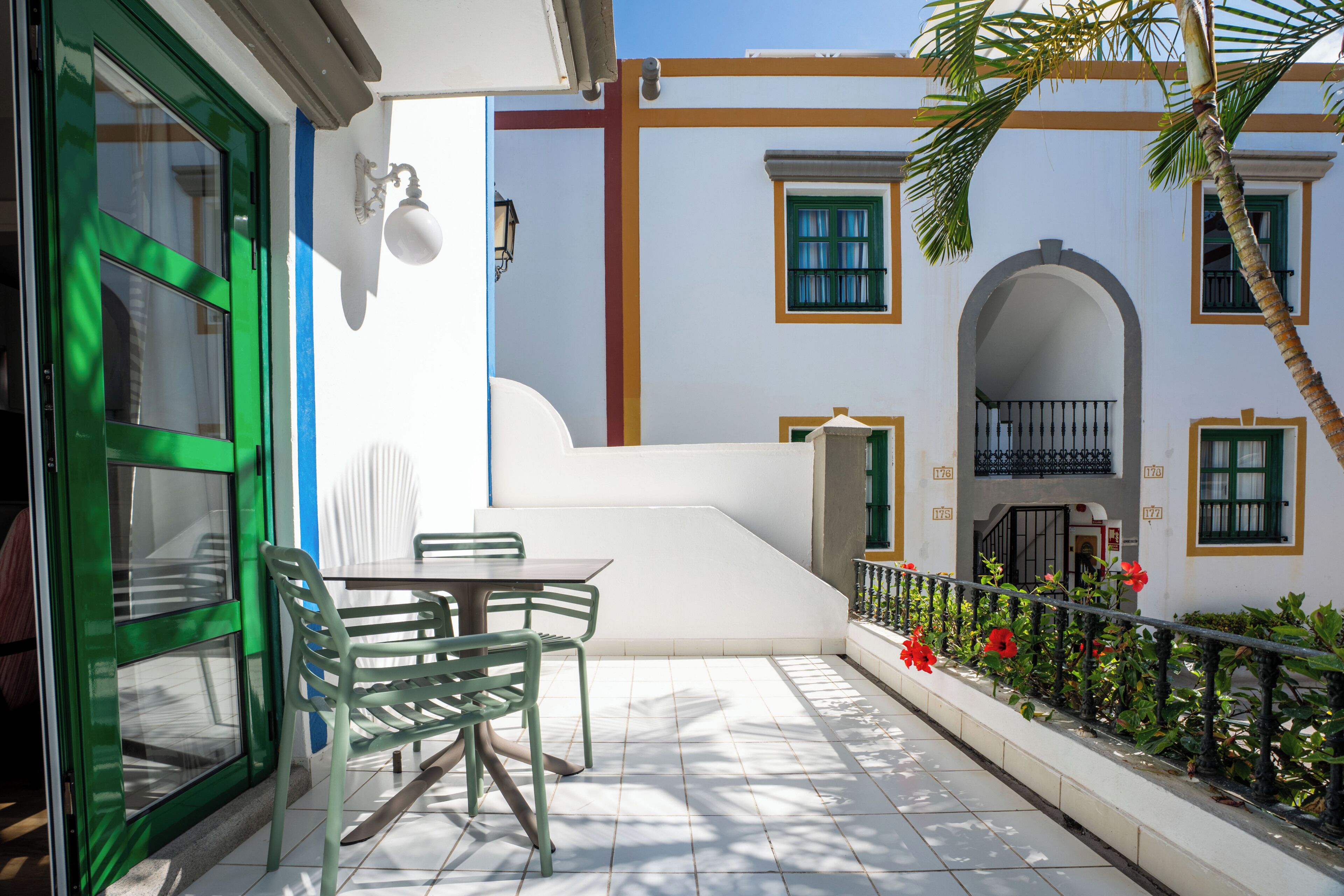 Une terrasse avec une table et des chaises, une porte verte et un bâtiment blanc doté de balcons et de fenêtres.