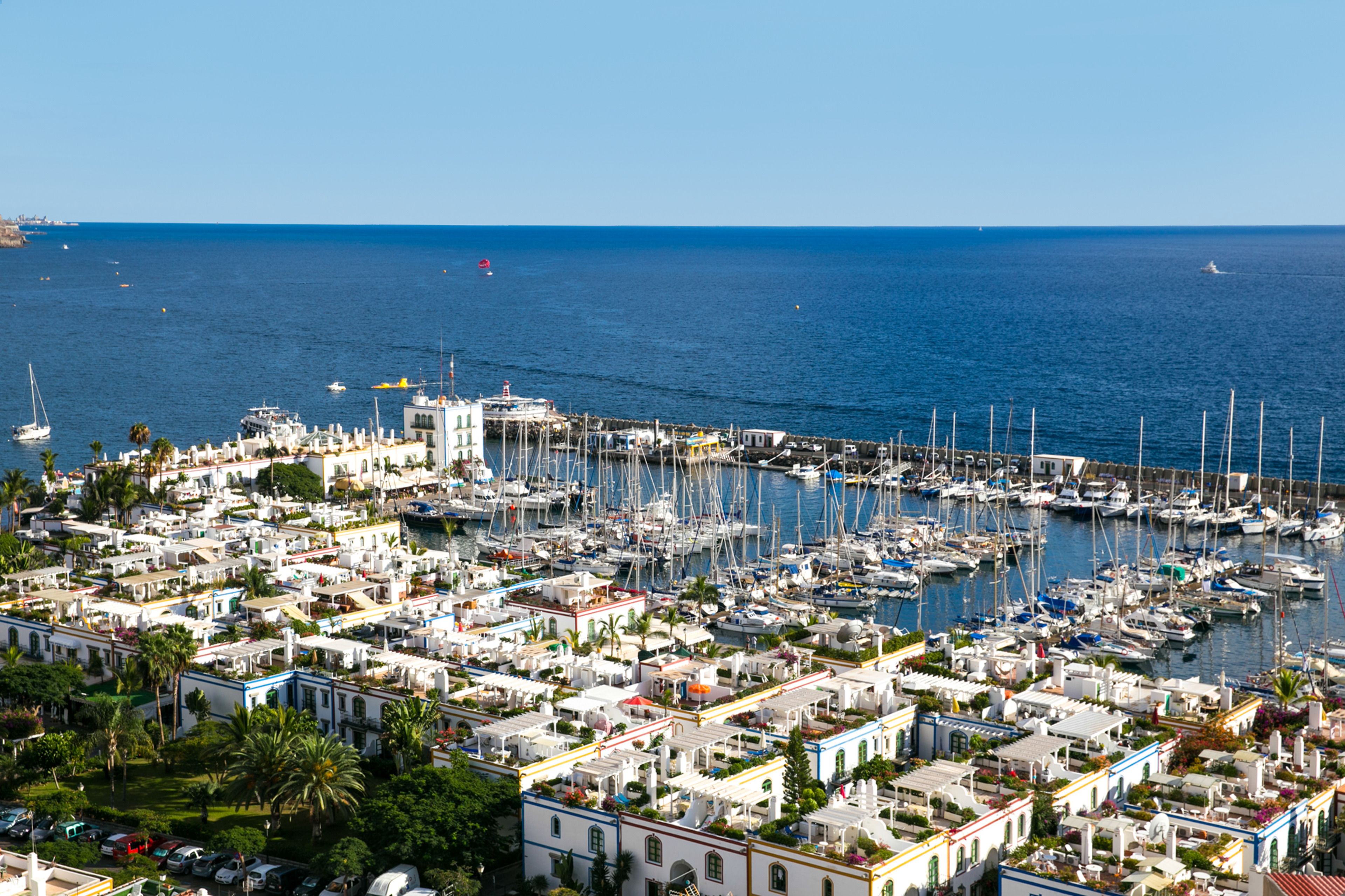 A marina filled with boats and a densely packed coastal town with white buildings and palm trees.