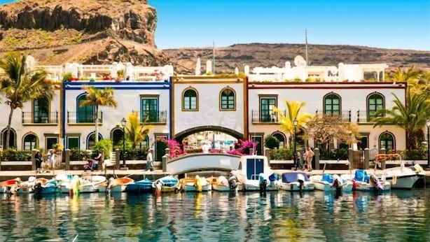 Un hôtel situé au bord de l’eau, avec une rangée de bâtiments aux couleurs vives, une colline rocheuse en arrière-plan et des bateaux amarrés sur l’eau.