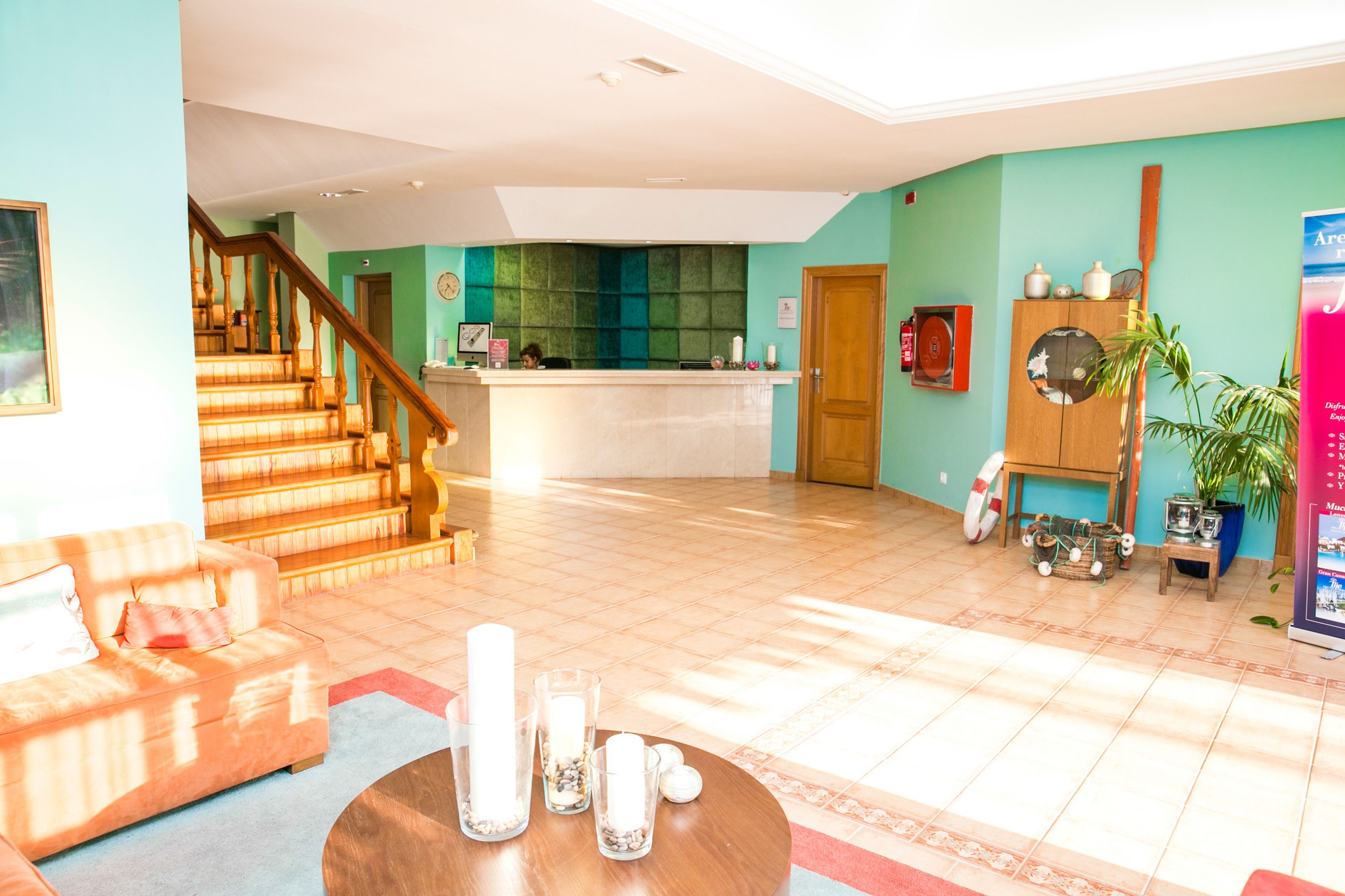 Un vestíbulo de hotel con mostrador de recepción, una escalera, un sofá, una mesa de centro y una planta en maceta.