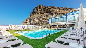 Un espace piscine avec des chaises longues, un bar et une vue sur des falaises rocheuses.