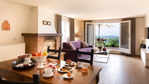 A dining area with a wooden table set for breakfast, a fireplace, a purple sofa, and a balcony with a view. - Tenuta Torre Rossa Farm & Apartments (Impruneta)