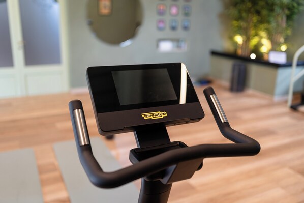 A stationary bike with a digital display and control panel, in a room with wooden flooring and a wall-mounted control panel. - Tenuta Torre Rossa Farm & Apartments (Impruneta)