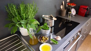 A modern kitchen with a built-in oven, a red coffee machine, fresh herbs, and a variety of cooking utensils. - Tenuta Torre Rossa Farm & Apartments (Impruneta)