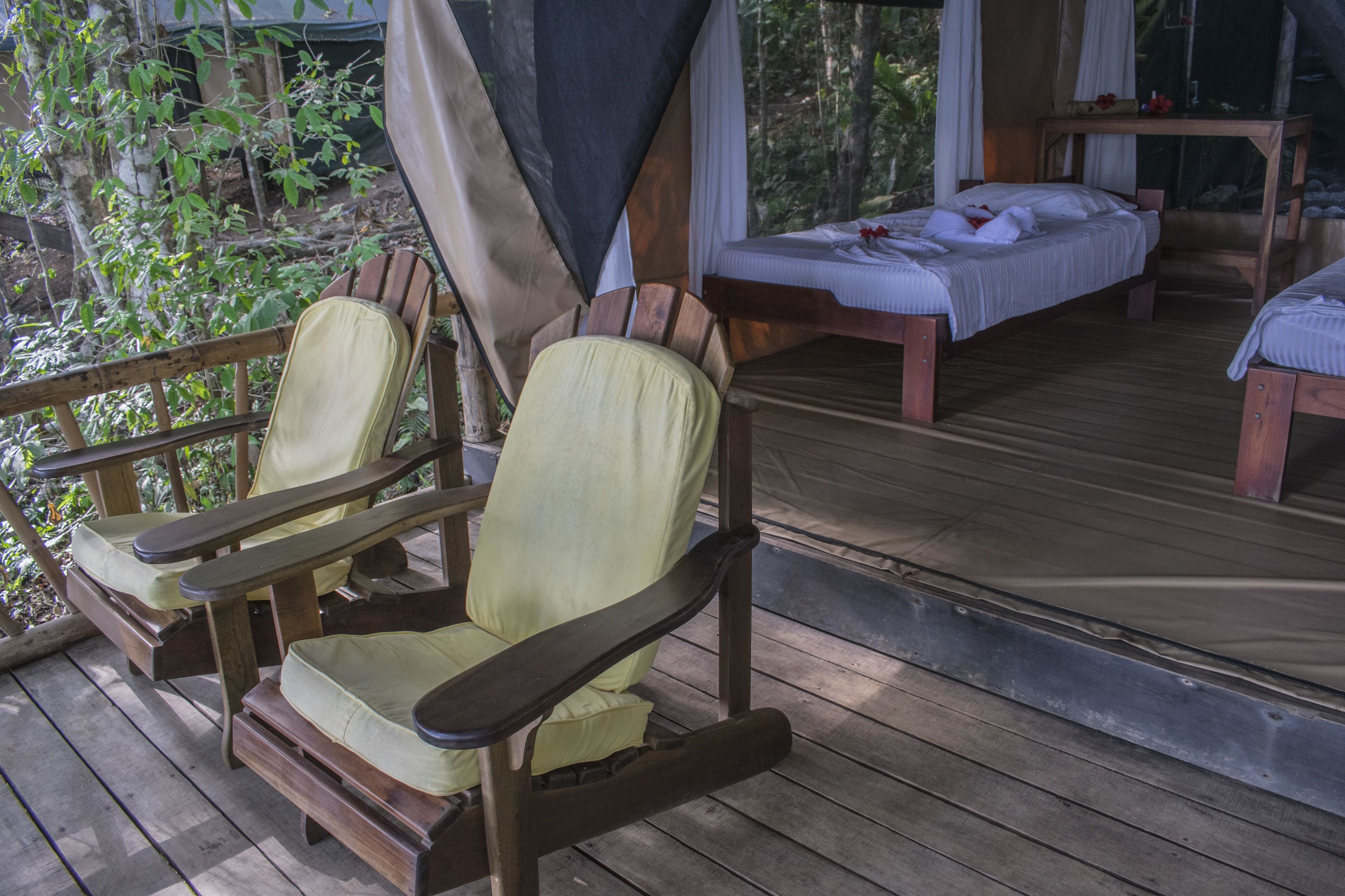 A wooden deck with two wooden chairs and a bed with white bedding.