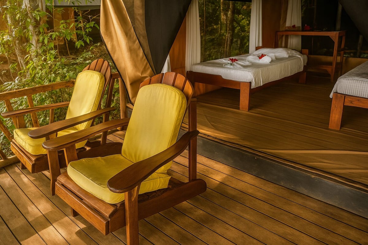 A wooden deck with two yellow cushioned chairs and a bed with white linens.