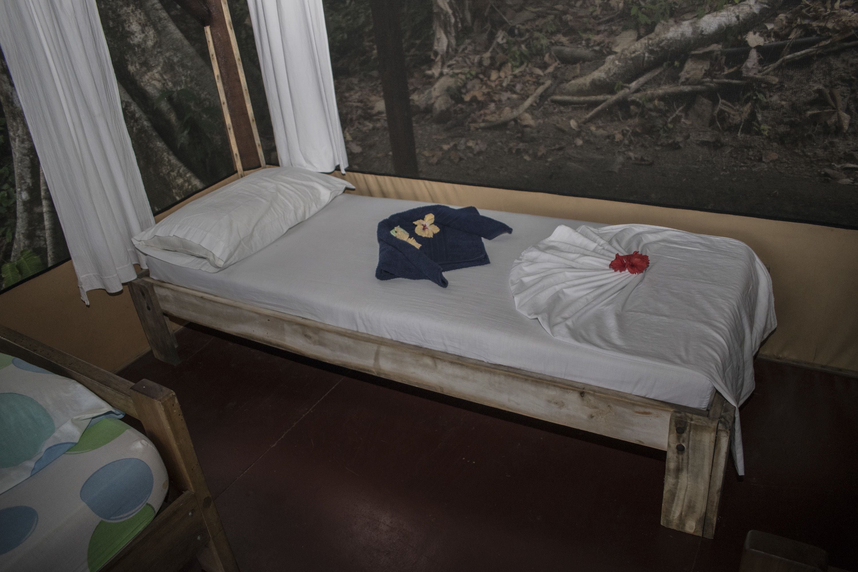 A single bed with a white mattress and a blue blanket, a white pillow, and a red rose.