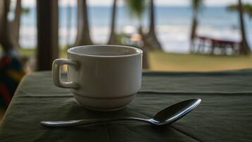 A white mug and spoon on a table with a view of the ocean and palm trees in the background.