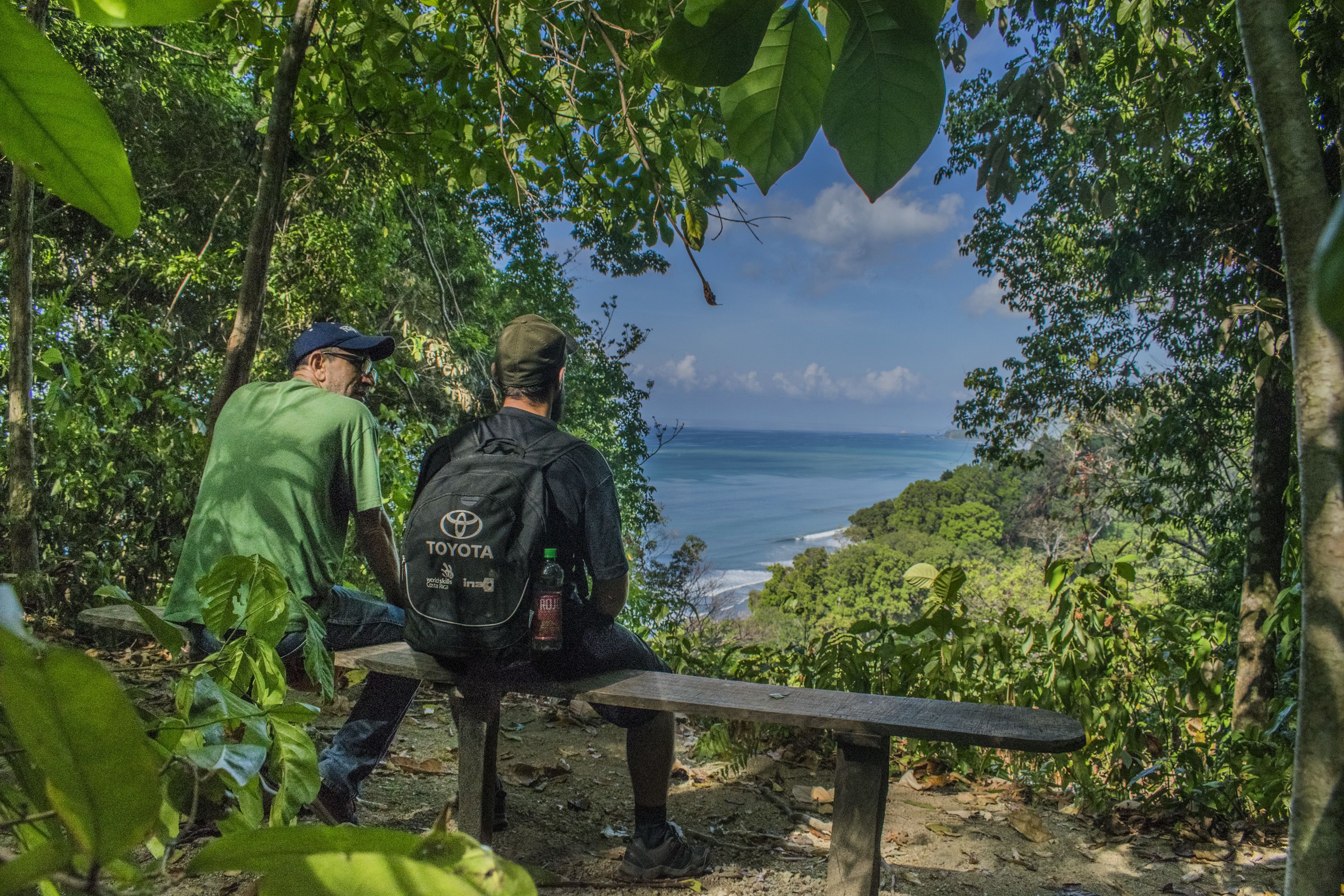 Deux personnes sont assises sur un banc, face à une vue sur la côte.