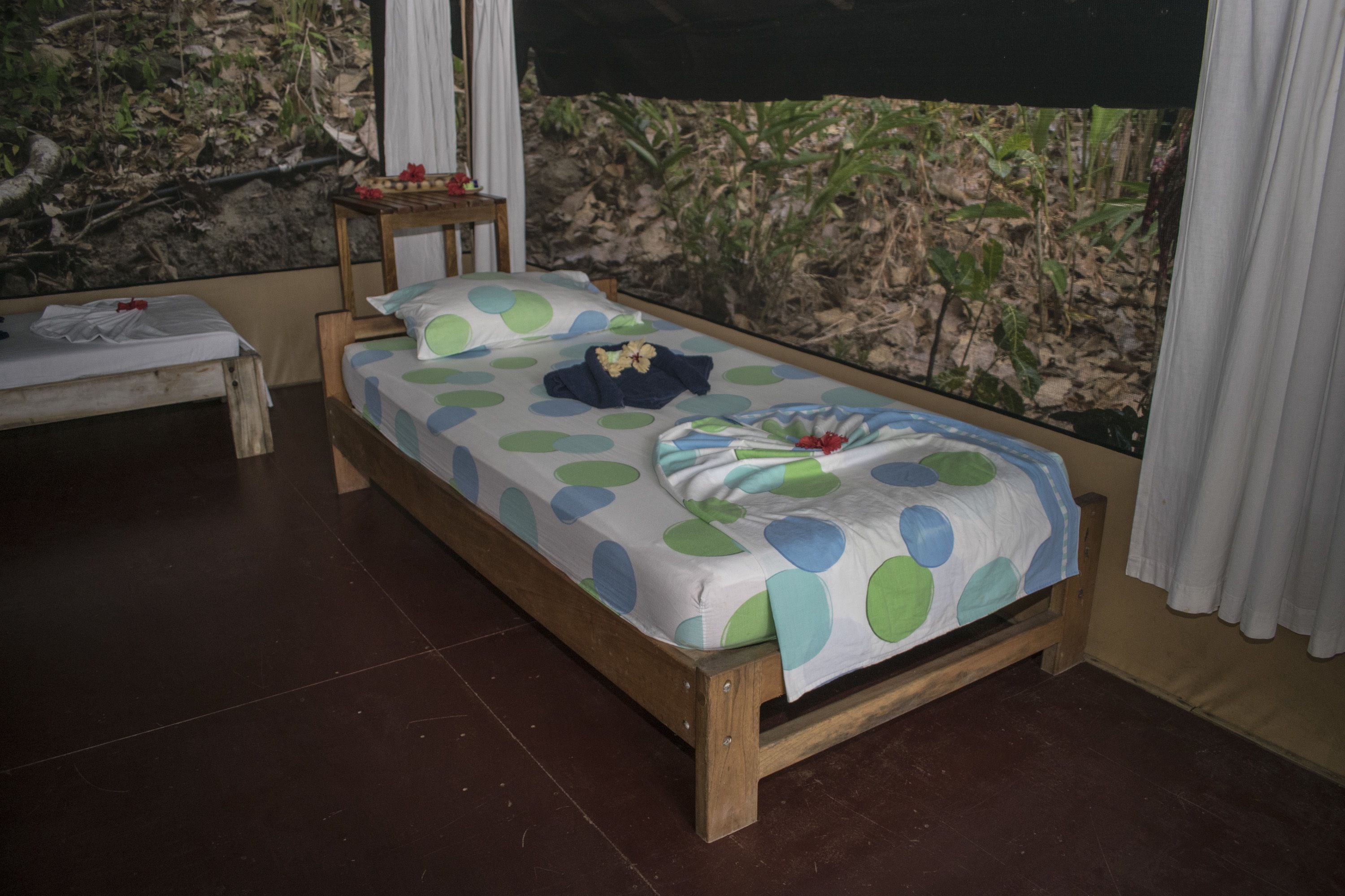 Un letto singolo con copripiumino a pois, una testiera in legno e un comodino con una lampada.