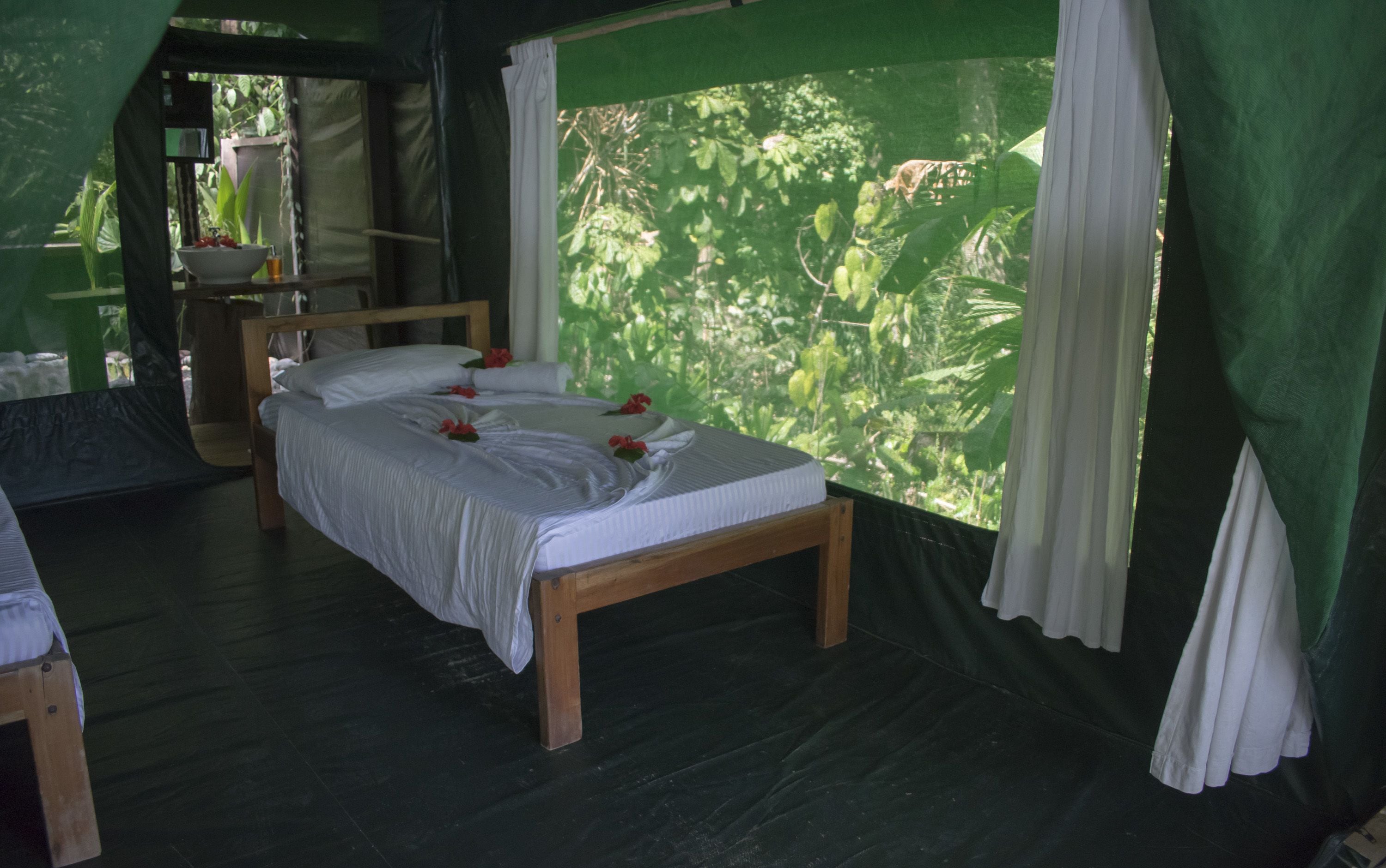 A room with a wooden bed, white linens, and a view of lush greenery through the window.