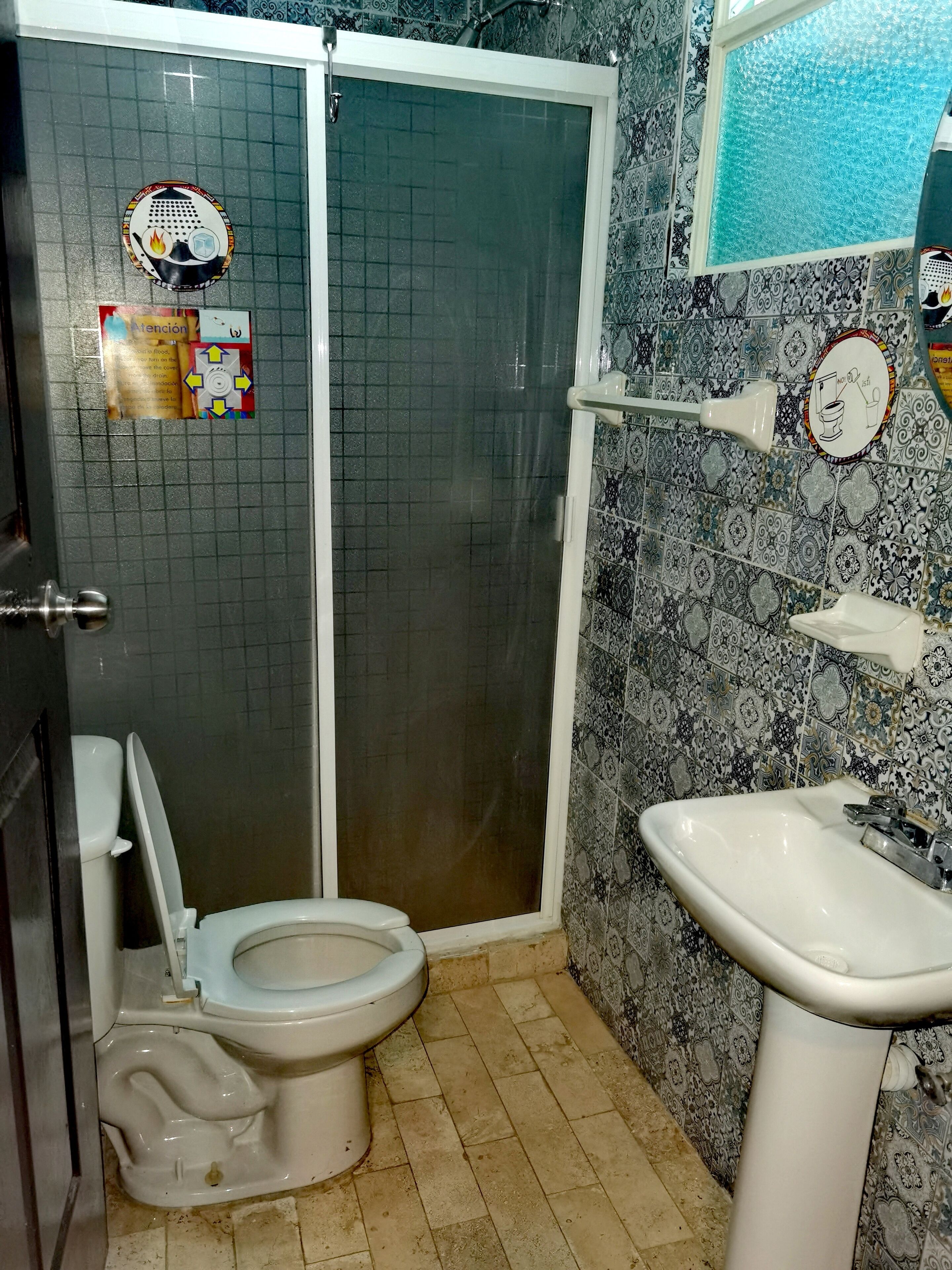 Un baño con inodoro, ducha y lavamanos. Las paredes están decoradas con azulejos y hay una ventana con panel esmerilado.