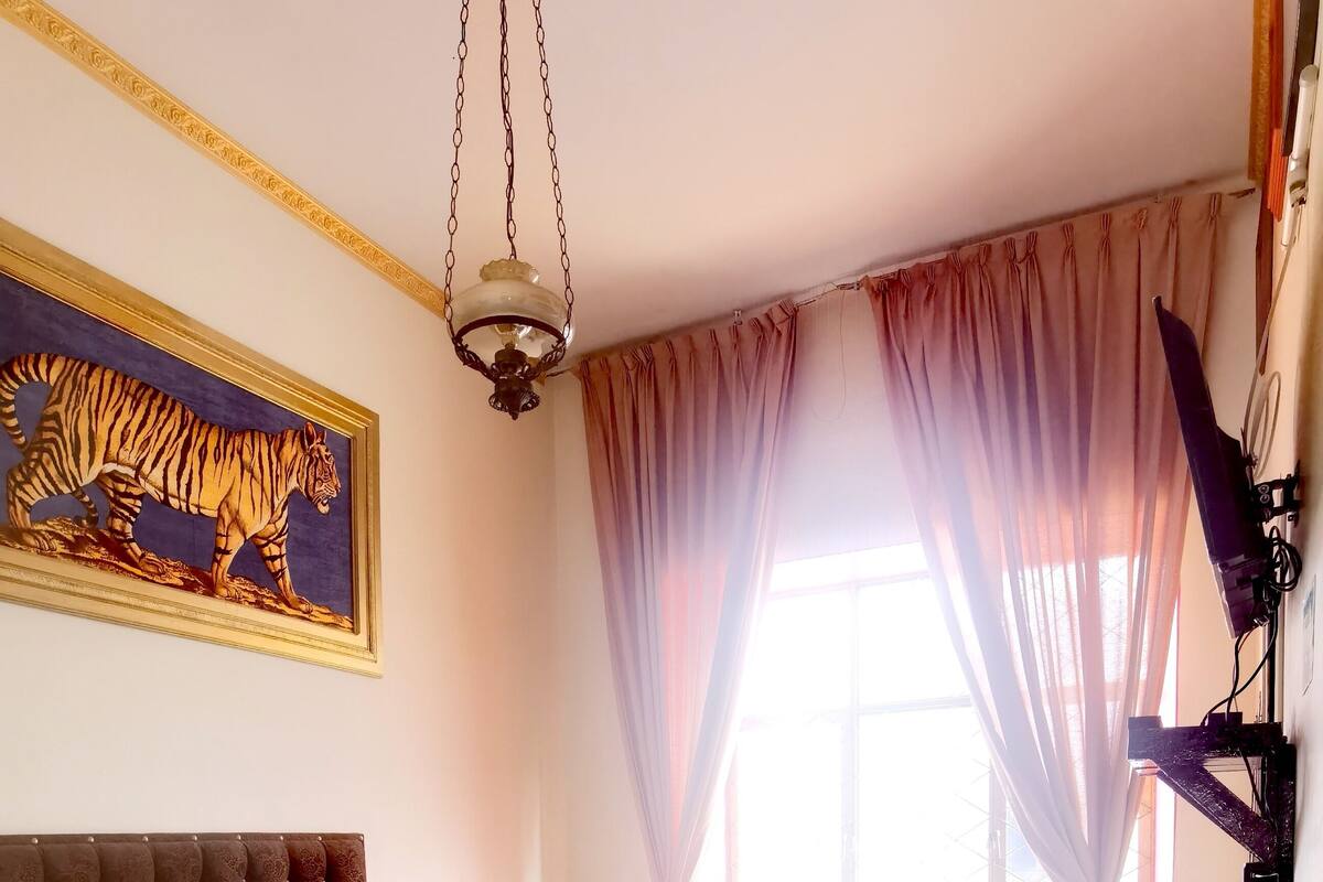 Camera da letto con un letto grande, un tavolino, una sedia, una lampada da terra e una finestra con tende.