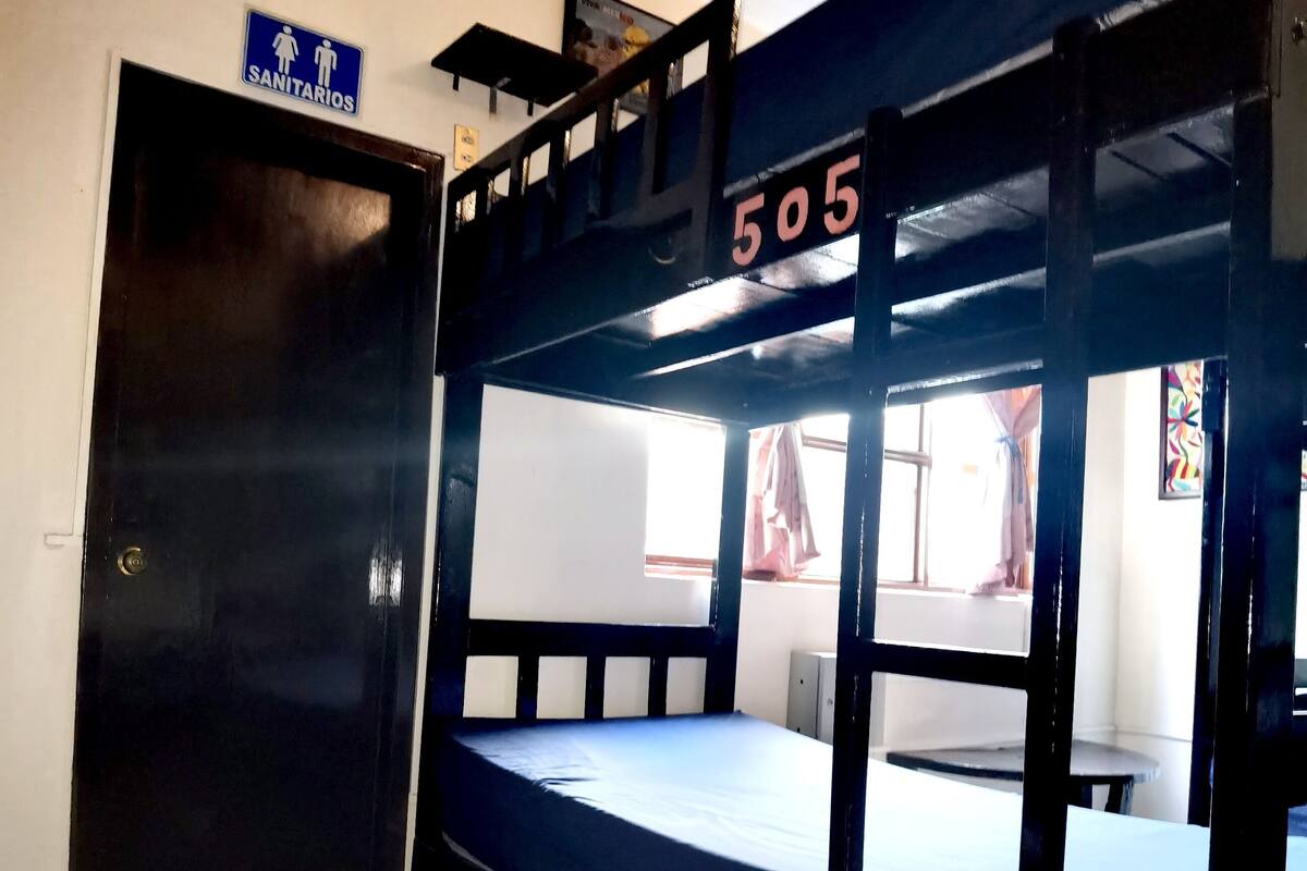Un letto a castello con il numero 505, una porta con l'indicazione 'SANITARIOS' e un piccolo tavolo con una sedia.