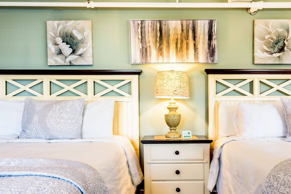 A hotel room with two beds, a nightstand with a lamp, and artwork on the walls.