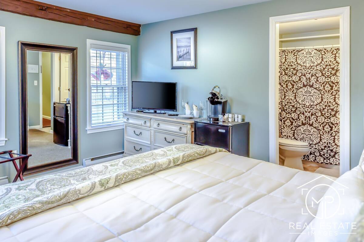 A bedroom with a bed, a dresser, a television, and a bathroom.