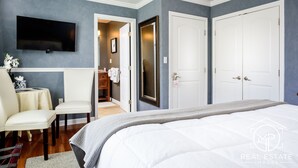 A bedroom with a bed, a TV mounted on the wall, a chair, and a small table with a vase of flowers. - Bouchard Inn (Newport)