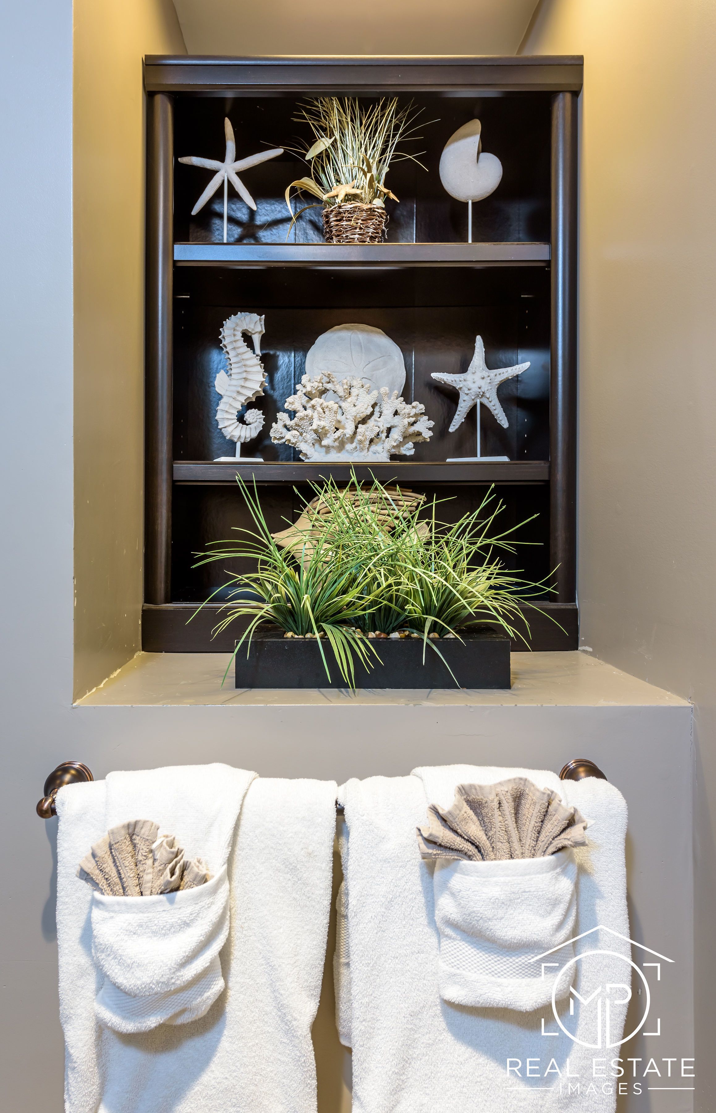 A bathroom with a shelf containing decorative items like starfish and shells, and towels with pockets.