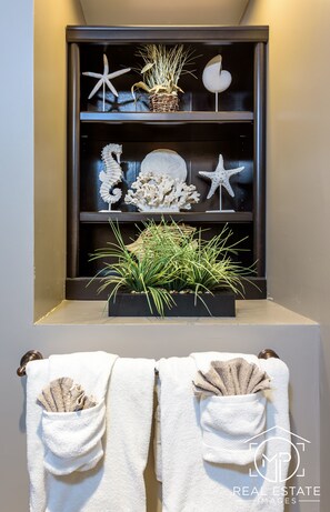 A bathroom with a shelf containing decorative items like starfish and shells, and towels with pockets.