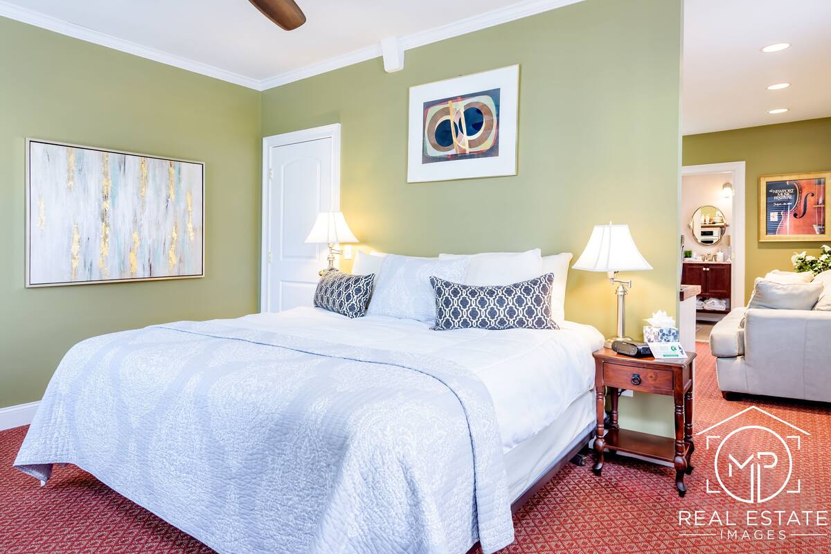 A hotel room with a large bed, two bedside tables, a nightstand, a mirror, and artwork on the walls.