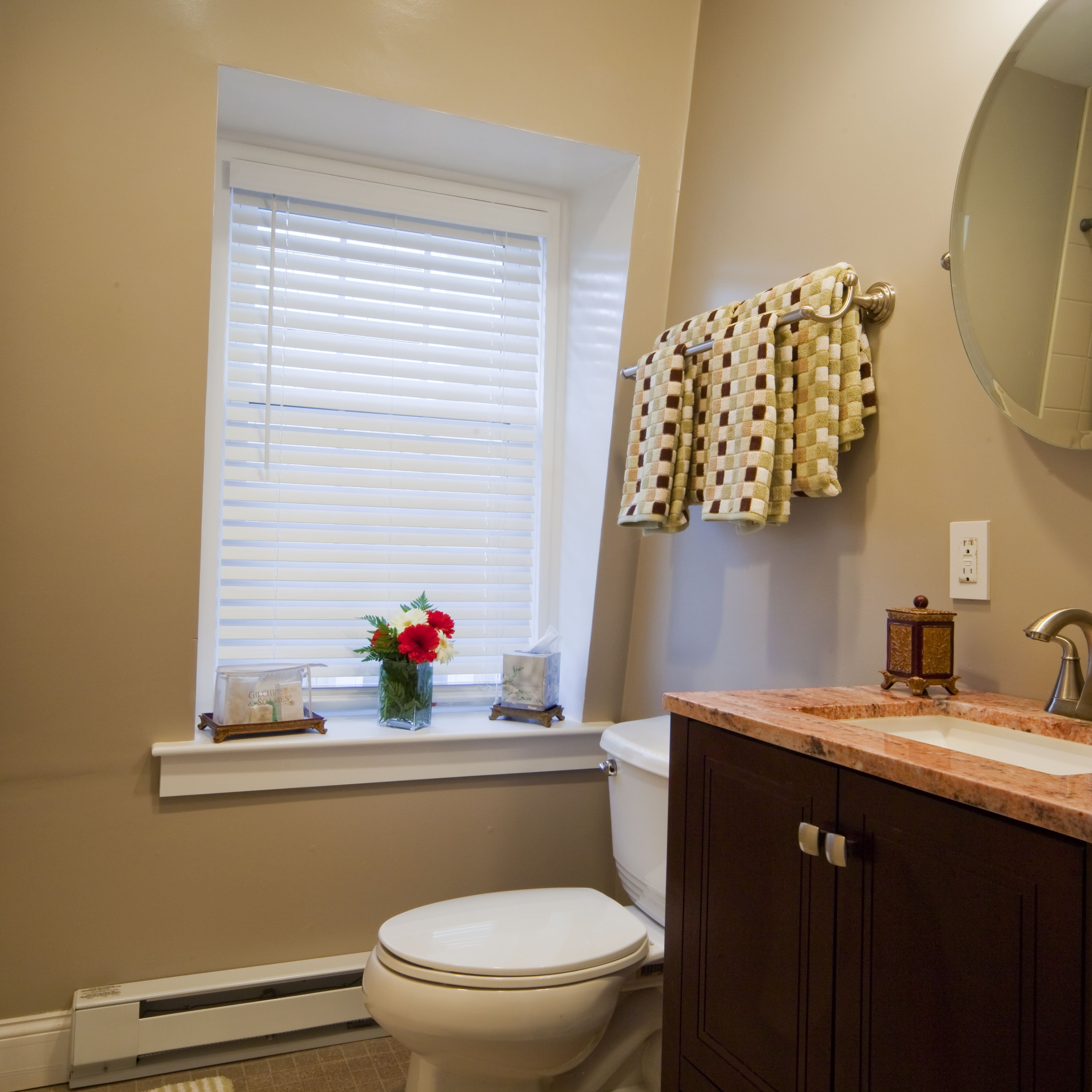 Une salle de bain comprenant des toilettes, une fenêtre avec des stores, un lavabo avec un plan de travail en marbre et un porte-serviettes avec des serviettes.