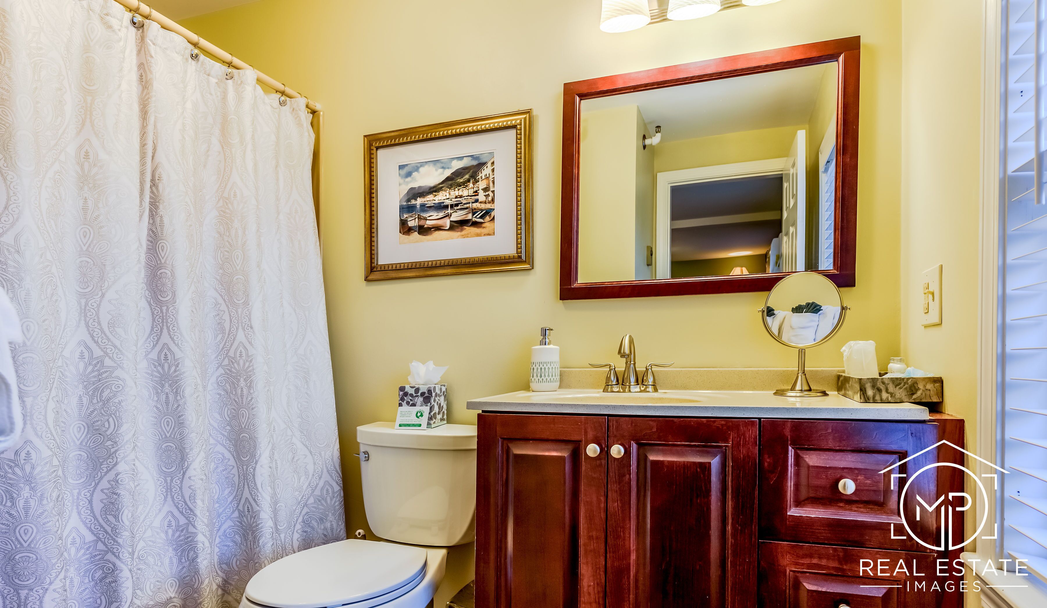 A bathroom with a toilet, sink, mirror, and a framed picture on the wall.