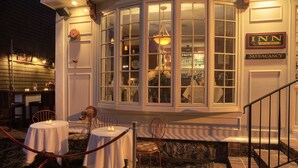 A corner of a building with a large window, a sign reading "INN NO VACANCY", and a table with chairs outside. - Bouchard Inn (Newport)