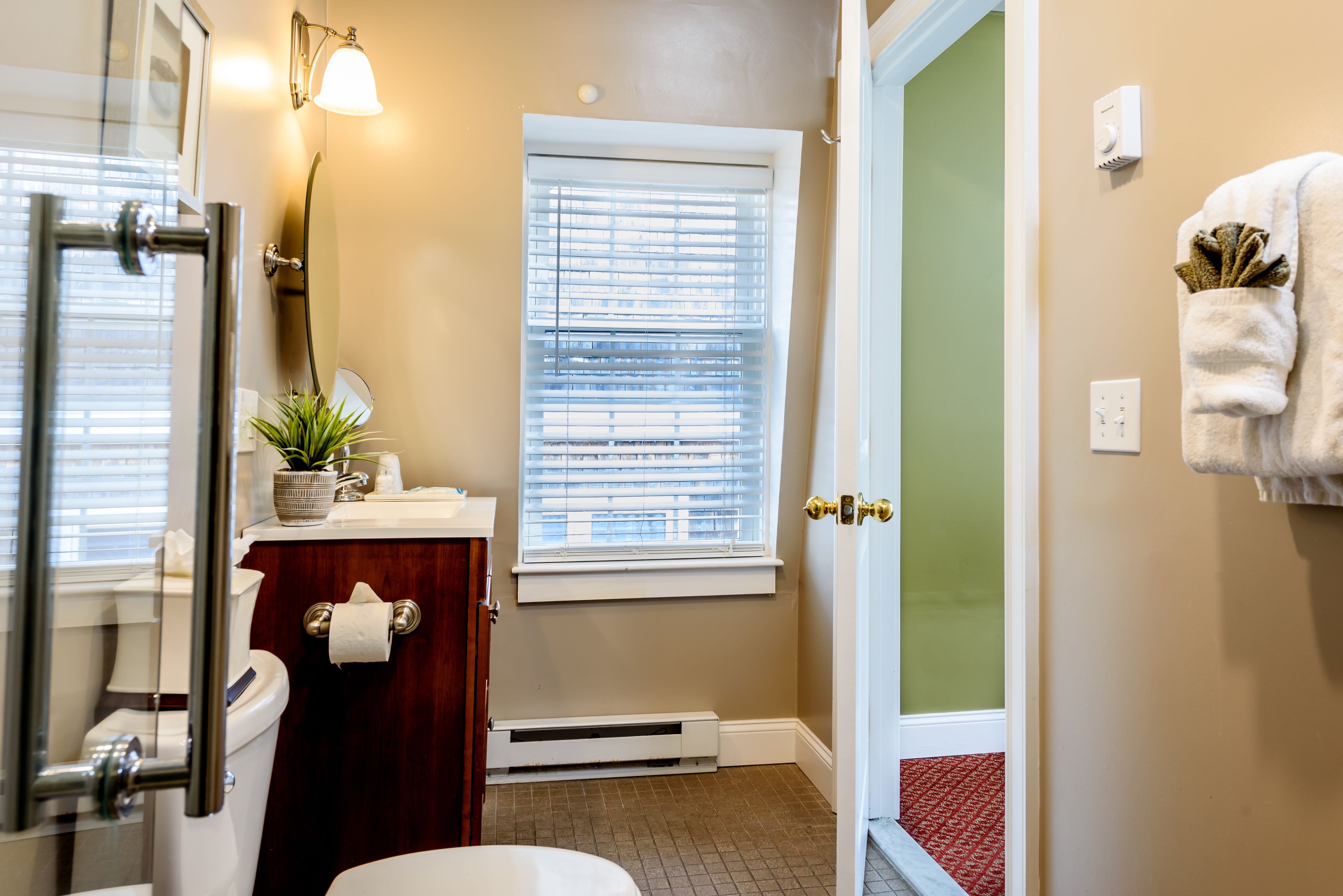 A bathroom with a toilet, bidet, towel rack, window with blinds, and a plant on the vanity.