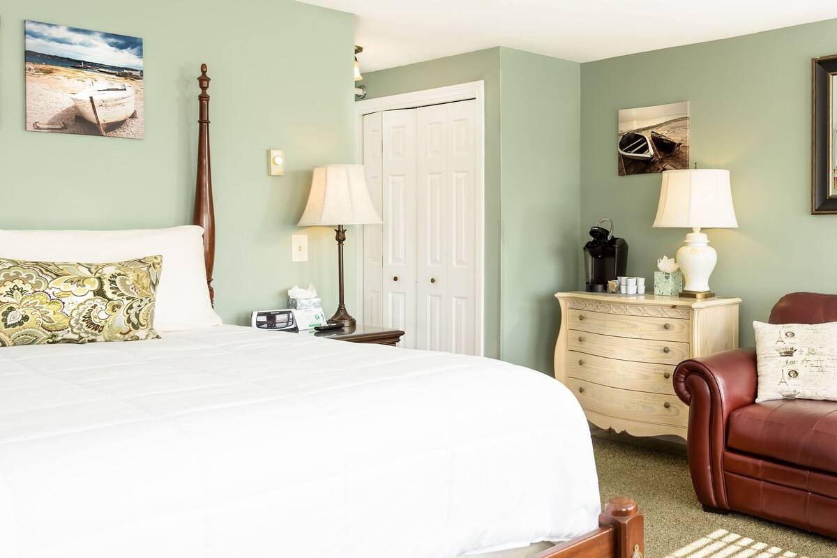 A bedroom with a bed, a dresser, a brown leather sofa, and two wall-mounted lamps.