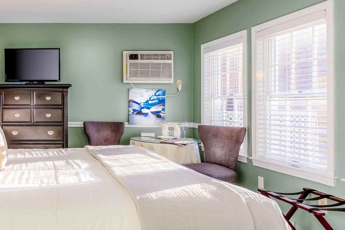 A neatly arranged bedroom with a bed, dresser, TV, and a painting on the wall.