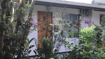 A building with a white exterior and a wooden door. There are various potted plants and flowers around the building.
