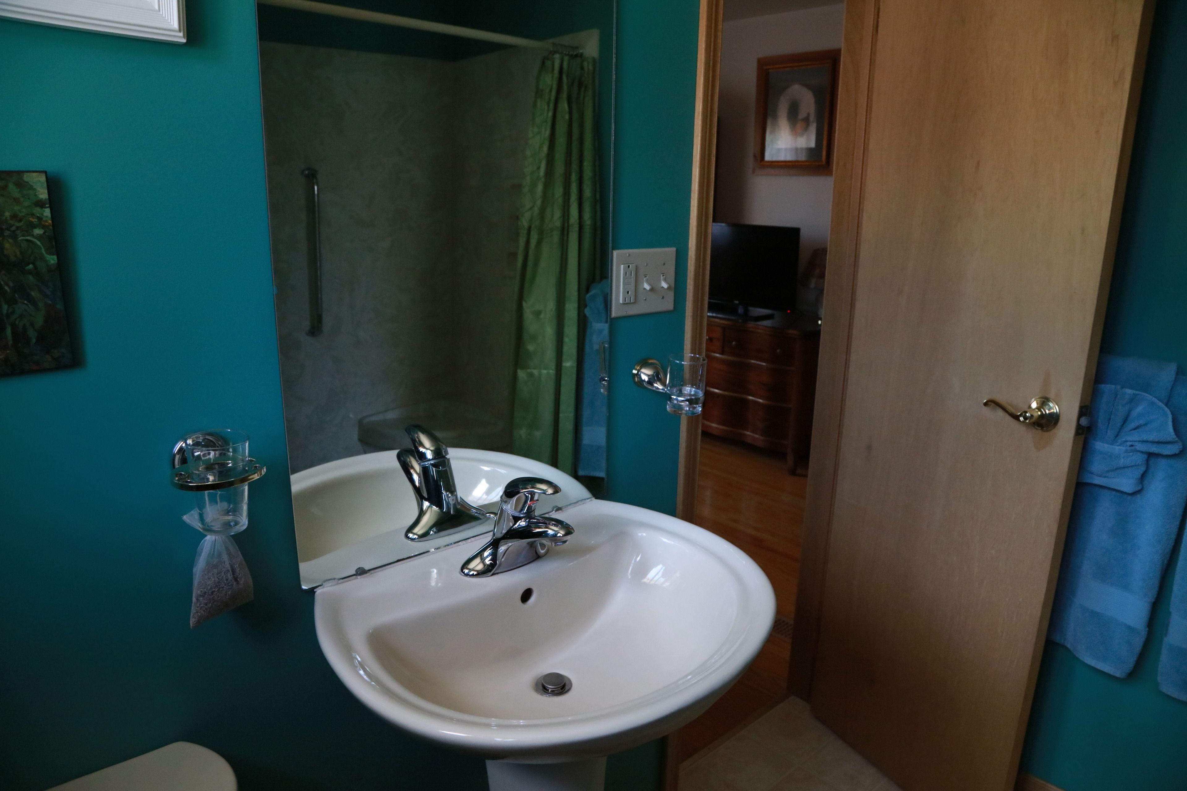 Une salle de bain avec un lavabo blanc, des murs verts et une porte en bois.