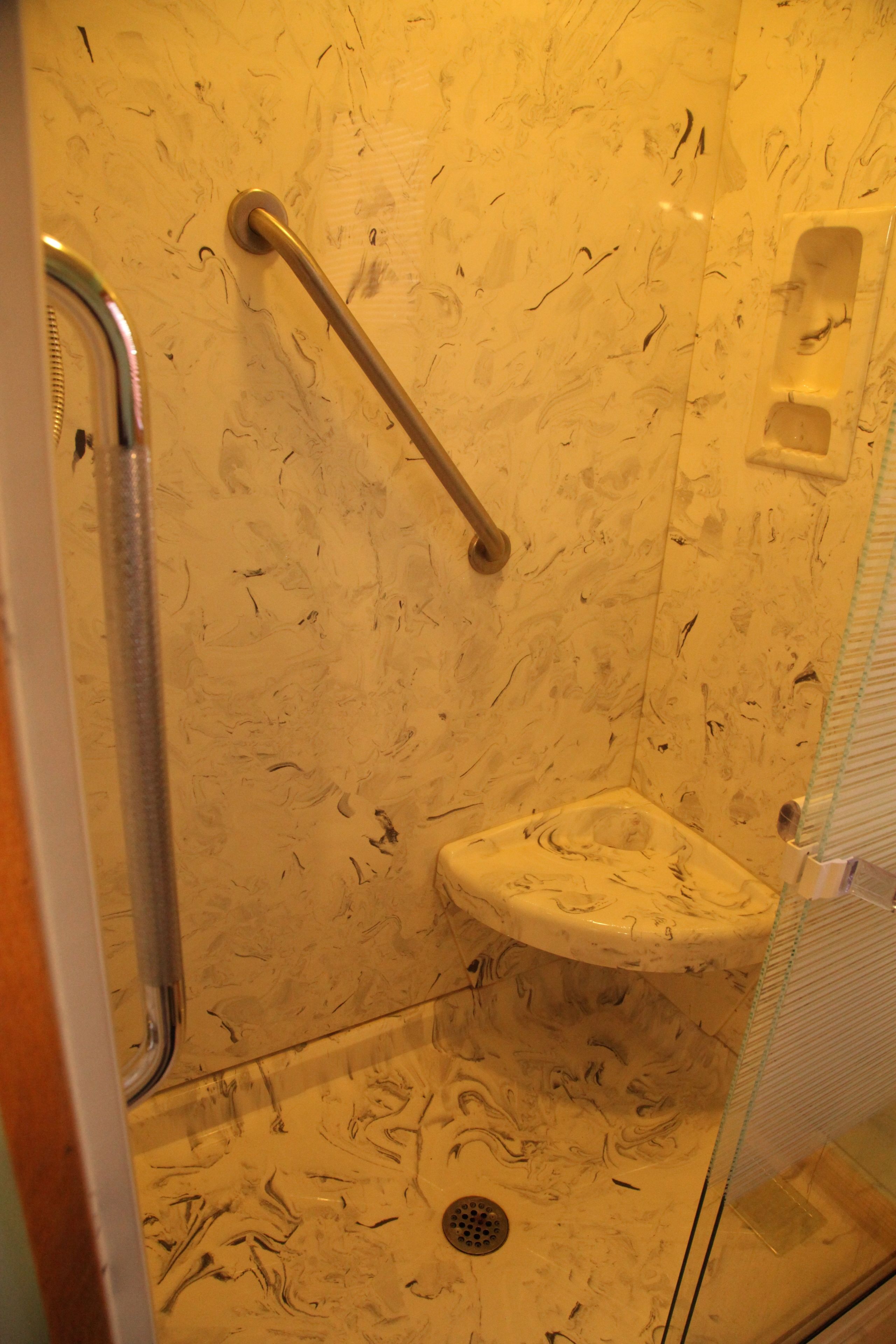 Een badkamer met een marmeren wand, een glazen douchecabine en een handgreep.