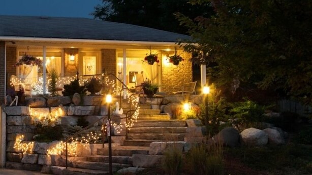 A stone house with a porch, outdoor lighting, and a staircase leading to the entrance. - A Garden Stroll B&B (Stratford)