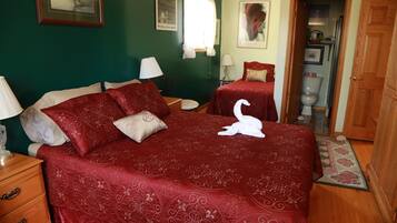 Quarto com uma cama grande, duas mesas de cabeceira, um guarda-roupa de madeira e um banheiro visível por uma porta aberta.