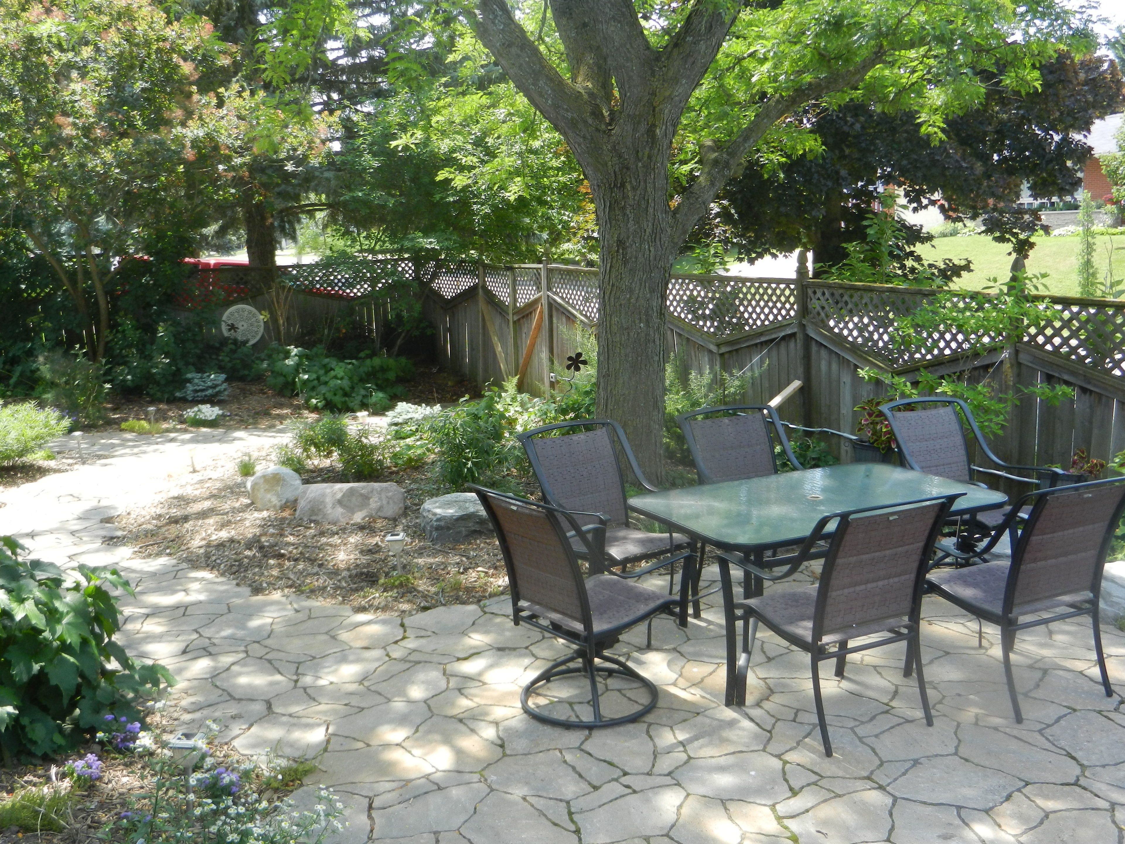 An outdoor patio with a table and chairs, surrounded by a garden and a wooden fence.