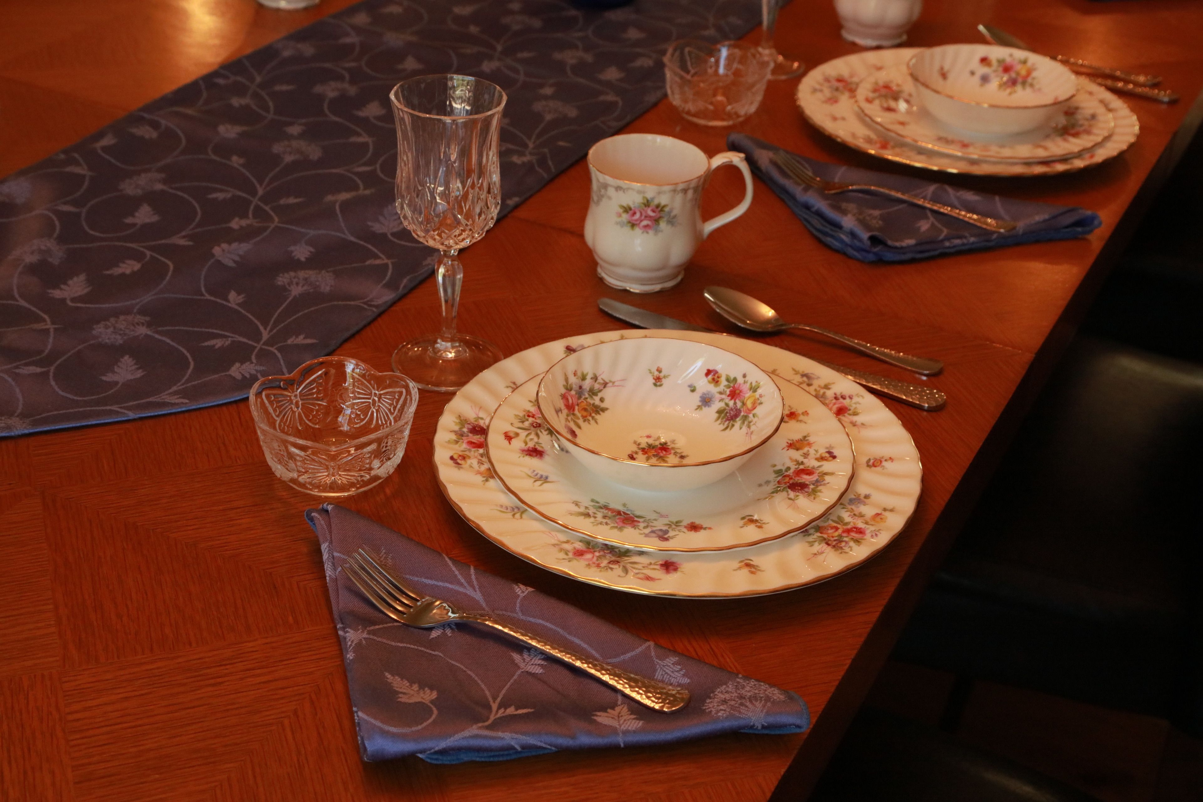A dining table set with floral-patterned plates, a glass, and cutlery.