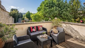 Terraza en la azotea con mobiliario de mimbre, una planta en maceta y vistas al verdor.