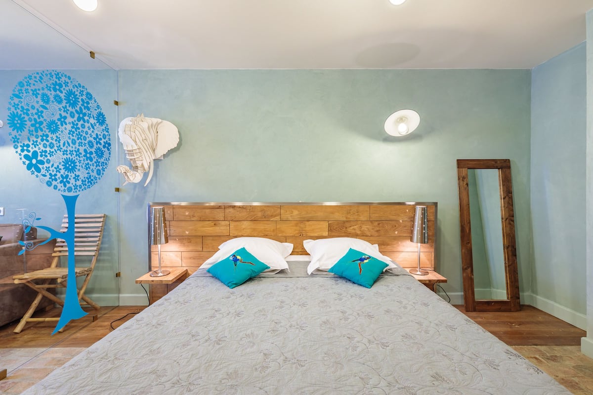 Une chambre à coucher avec une tête de lit en bois, deux oreillers blancs, un oreiller turquoise, un miroir et un élément décoratif mural.