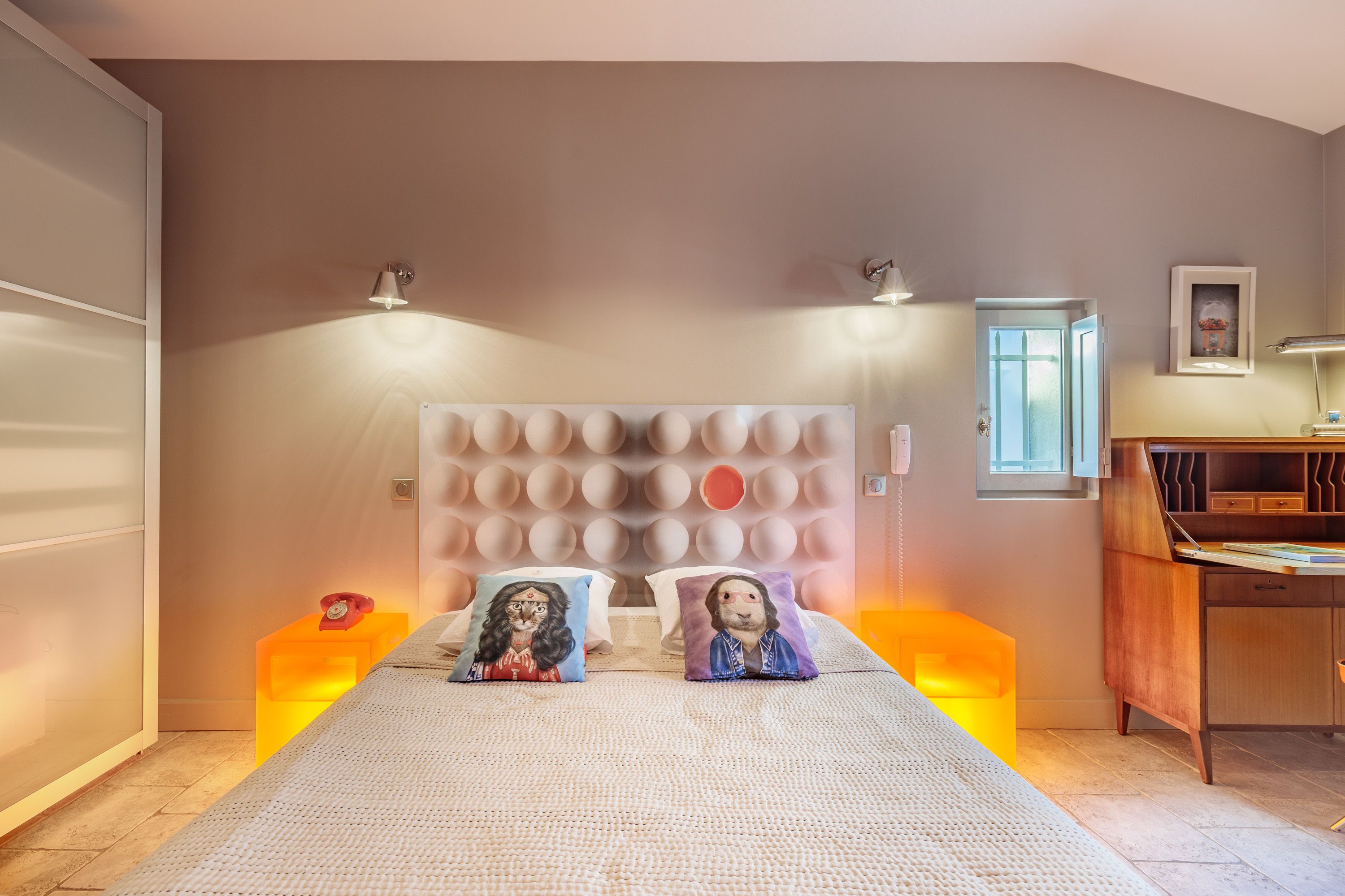 A bedroom with a large bed, two bedside lamps, a wooden desk, and a window.